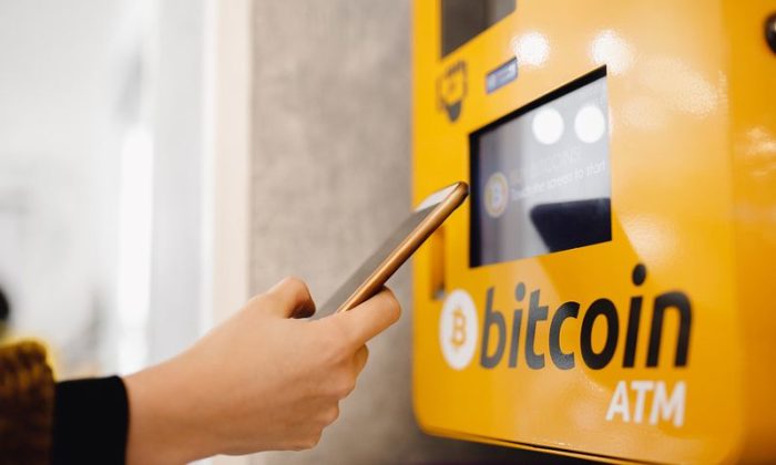 A person holding a phone in front of Bitcoin ATM machine to do some transactions